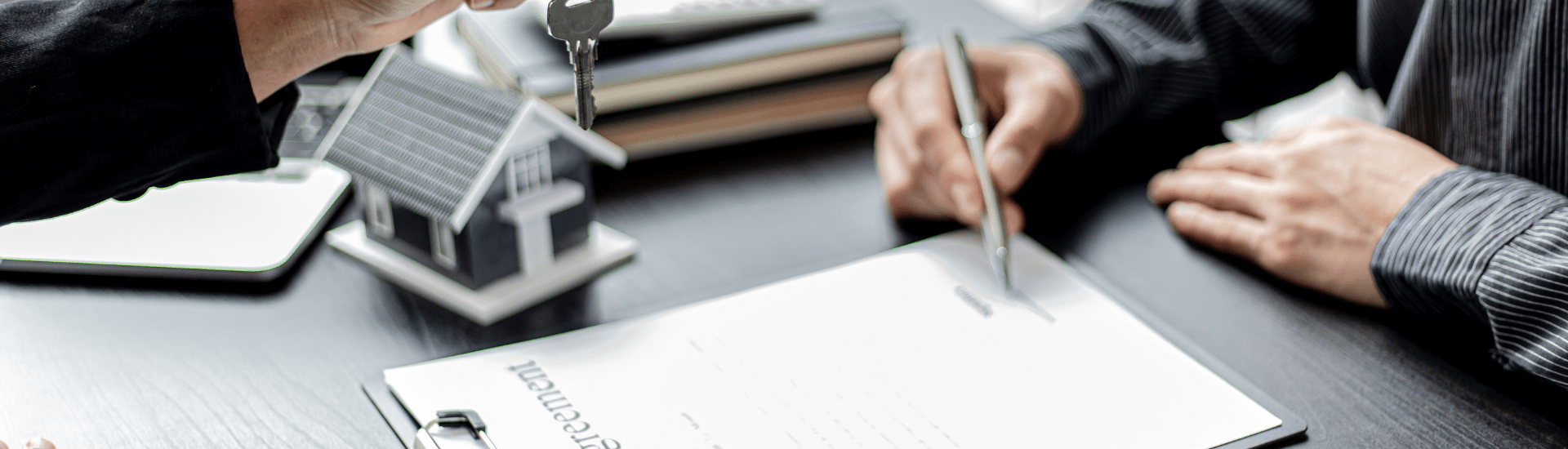 Mano che firma un contratto a canone concordato su una scrivania, con penna e documenti in primo piano.