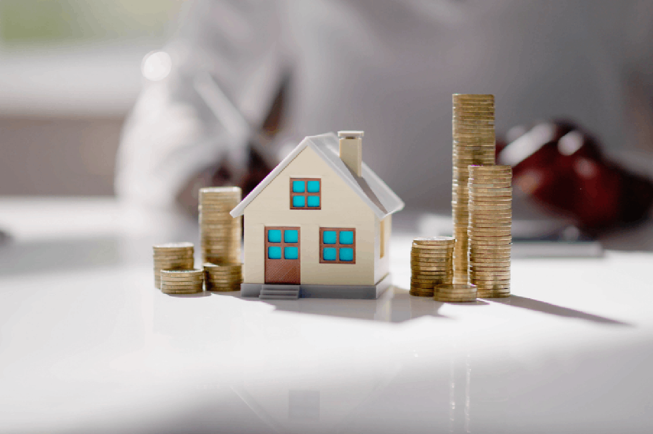 Casa in miniatura accanto a pile di monete, simbolo del contratto di locazione a canone libero.