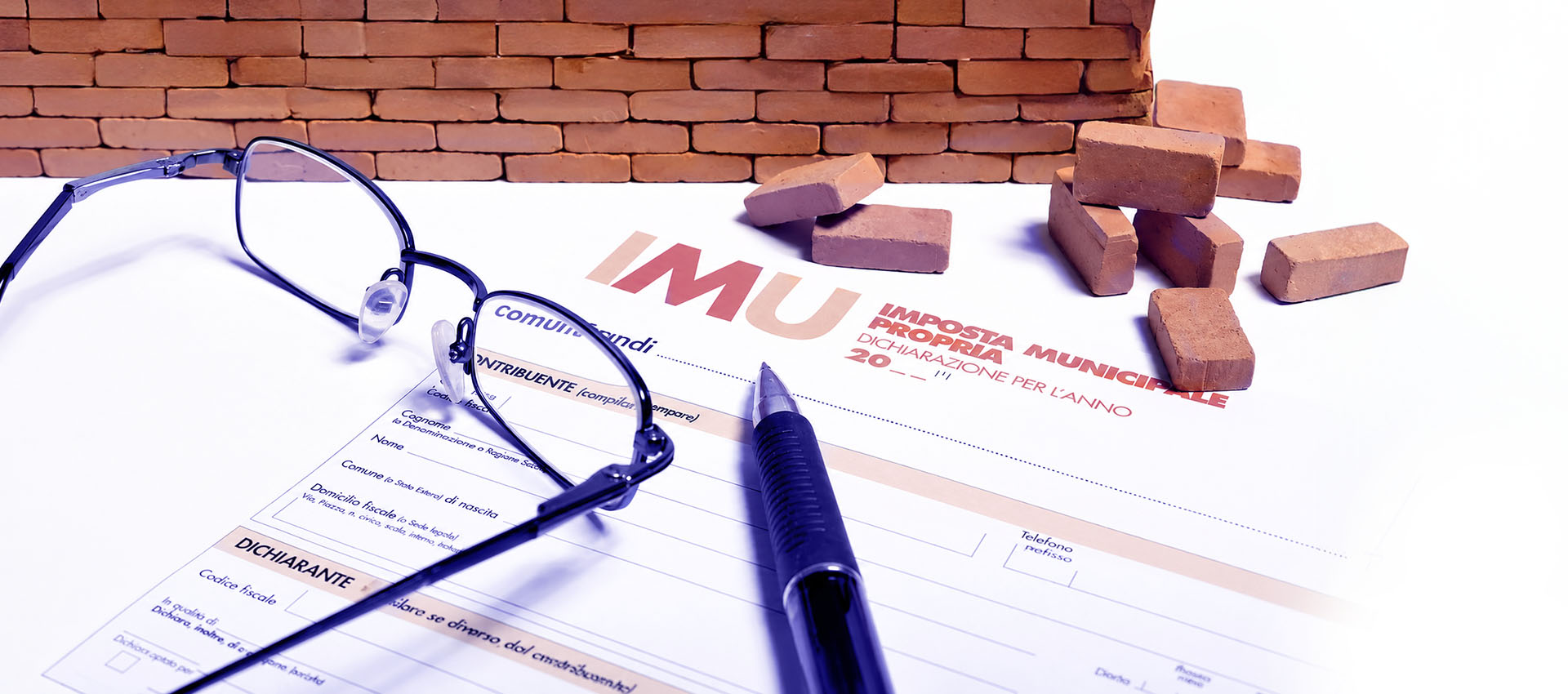 Modulo fiscale per il pagamento dell’IMU accanto a elementi simbolici come occhiali, penna e mattoni che rappresentano la tassazione degli immobili.