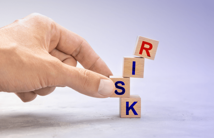 Mano che tiene in equilibrio quattro cubetti di legno con la scritta RISK, simbolo del rischio locativo negli investimenti immobiliari